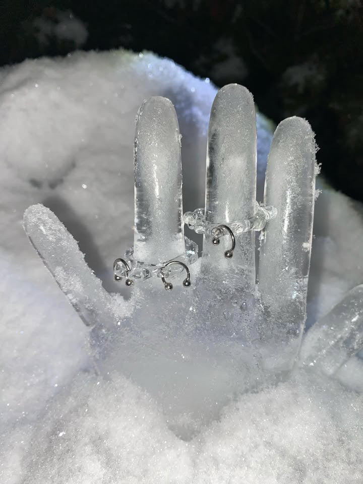 Organic Pierced Glass Ring 0062 in clear hand-sculpted borosilicate glass, shown on a hand cast in ice, Rain and Rivers