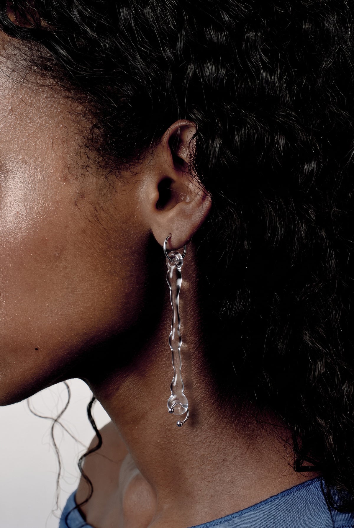 Drop Earrings 0004 in clear hand-sculpted borosilicate glass with a stainless steel piercing, worn on the ear, Rain and Rivers
