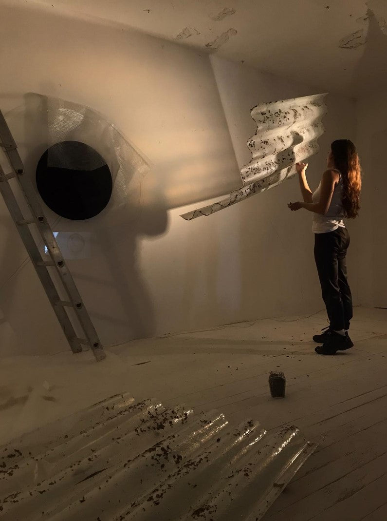 Artist Magdalena Hart working on a glass and light installation, shadows cast across the gallery wall