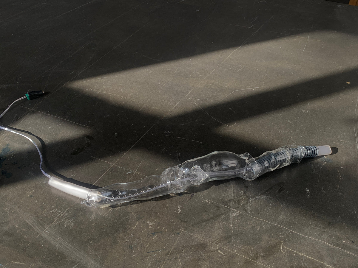 Long blown glass sculpture lying in a strip of sunlight on a dark floor