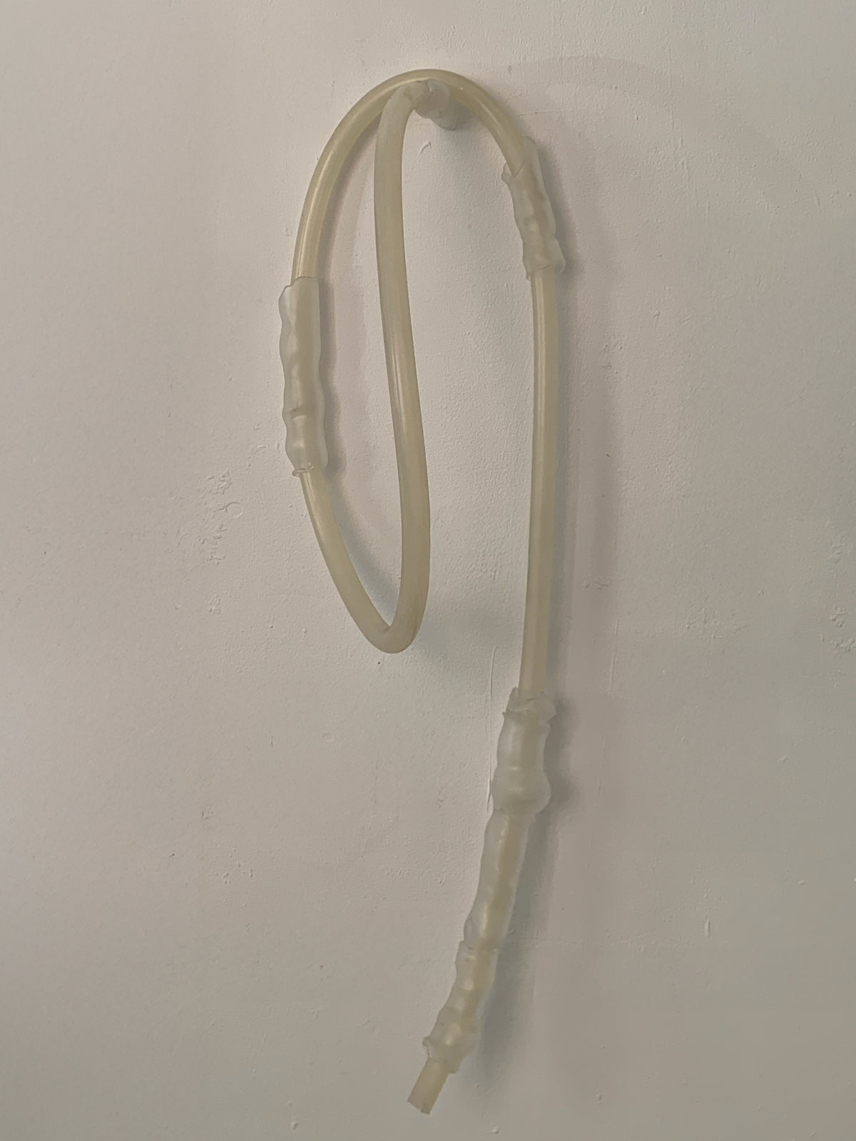 Looped borosilicate glass sculpture with hand-formed joints on a white wall